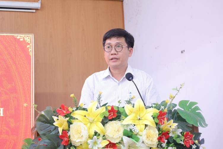 'A person standing at a podium with a microphone and flowersAI-generated content may be incorrect.'